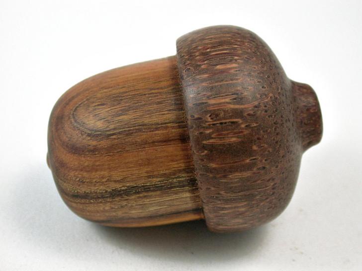 a close-up photo of a wooden object shaped like an acorn, with visible wood grain and a cap, set against a plain white…