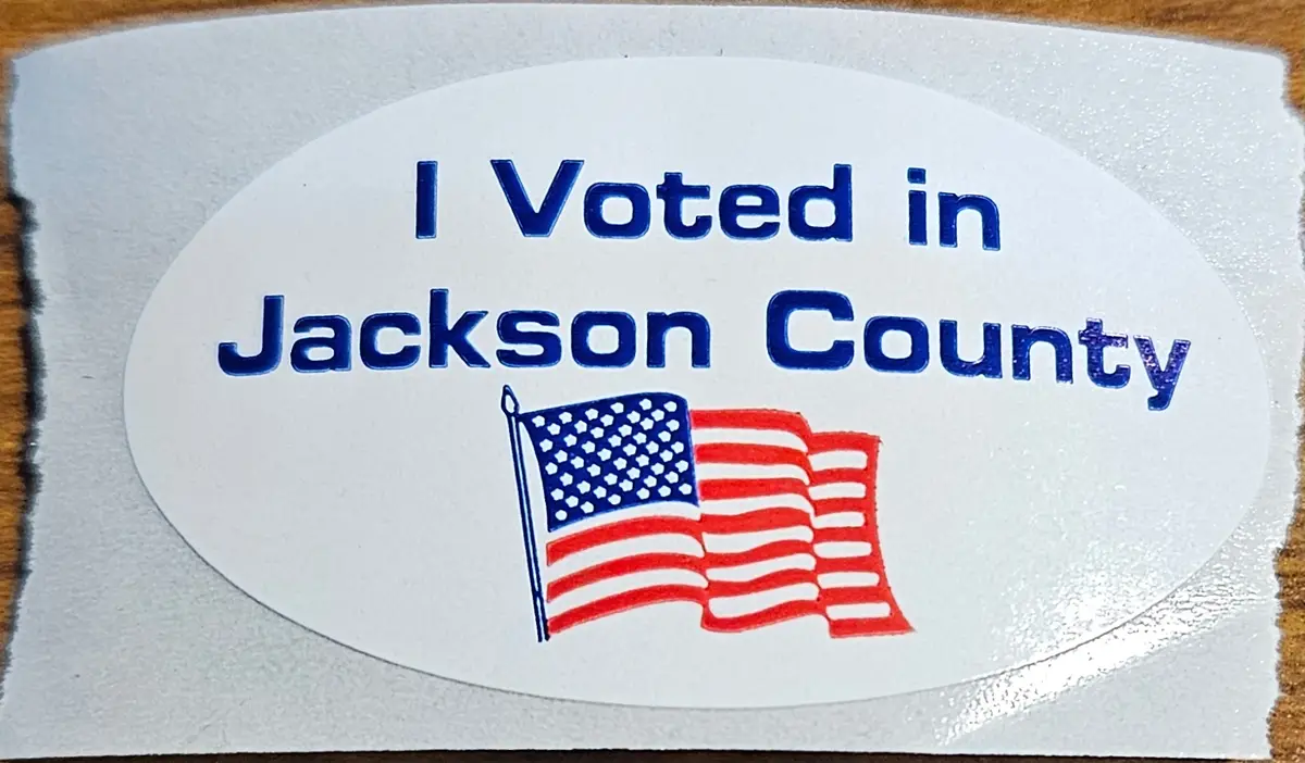 A close-up photo of a white oval sticker with blue text reading 'I Voted in Jackson County' and a hand-drawn American flag…
