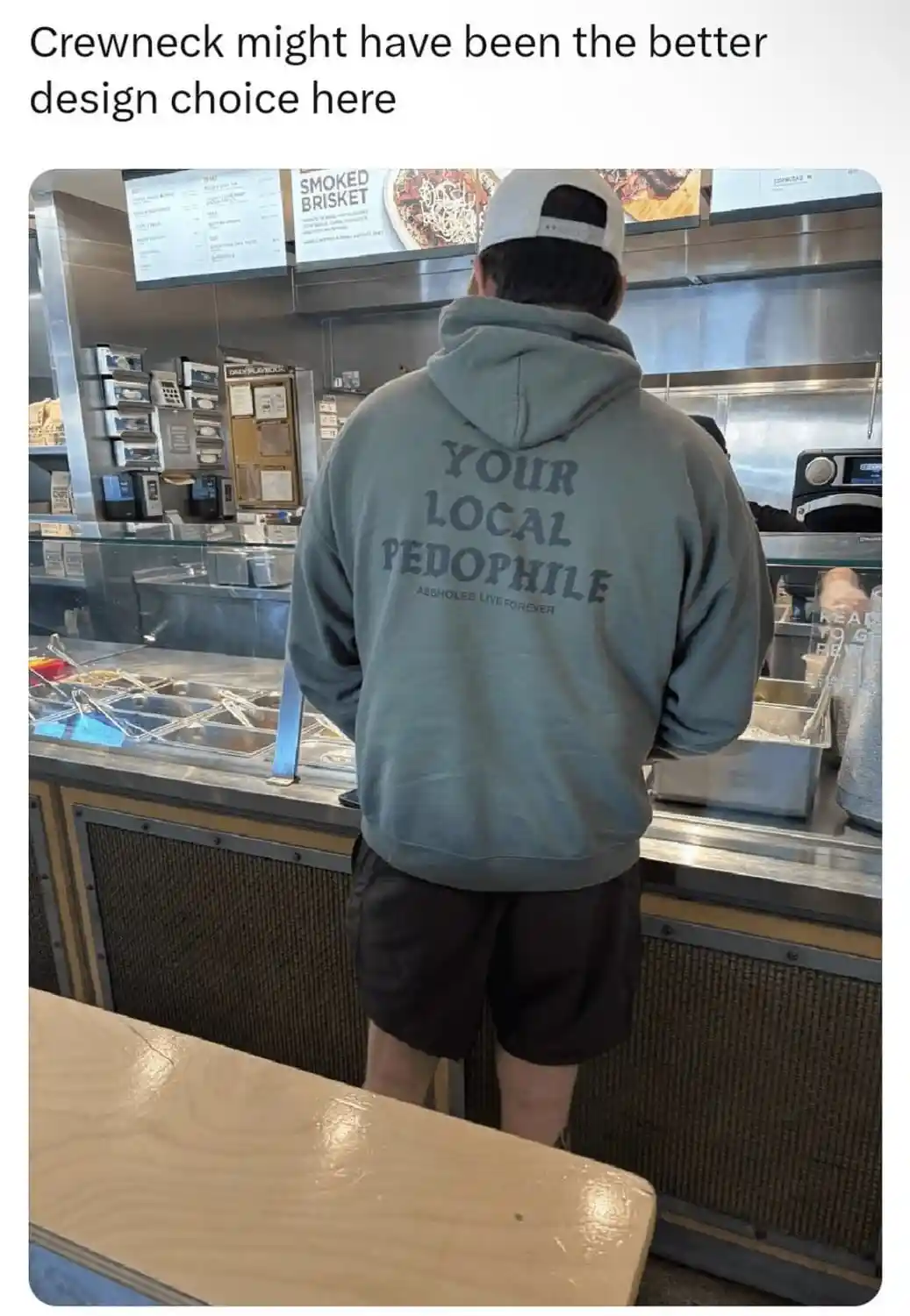A person wearing a grey hoodie with the text 'YOUR LOCAL PEDOPHILE' and 'ASSHOLES LIVE FOREVER' on the back stands at a food…
