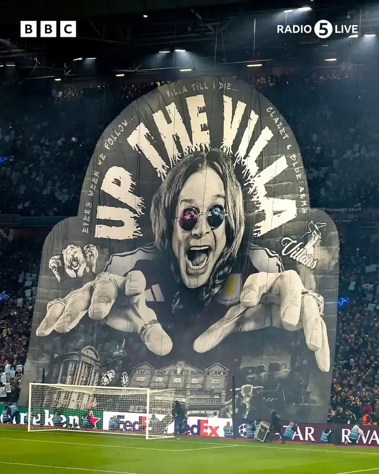 A massive black-and-white tifo banner at a football stadium features a stylized image of Ozzy Osbourne wearing sunglasses…