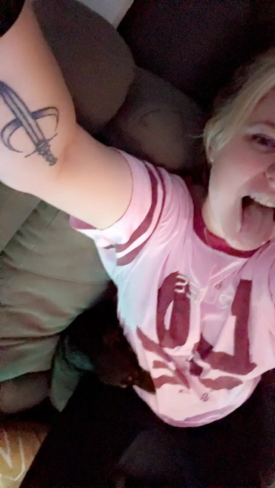 A person with blonde hair, wearing a pink and white striped shirt, is taking a selfie while enthusiastically showing off a…