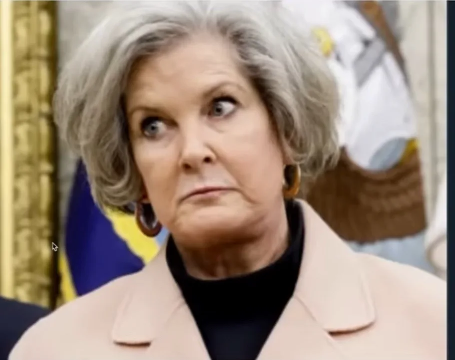 a close-up of a woman with gray hair and a beige coat, looking upward and to her right with a skeptical, confused…