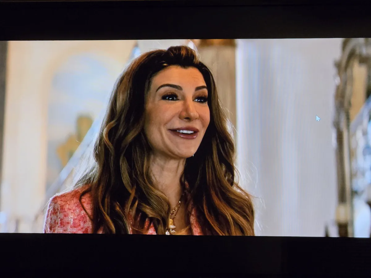A woman with long brown hair and a pink top smiles while wearing a white veil, likely in a wedding scene. A computer mouse…