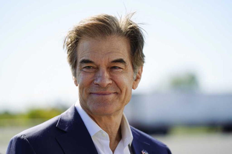 a close-up photo of a smiling middle-aged man with graying hair wearing a dark suit and white shirt. The image has text…