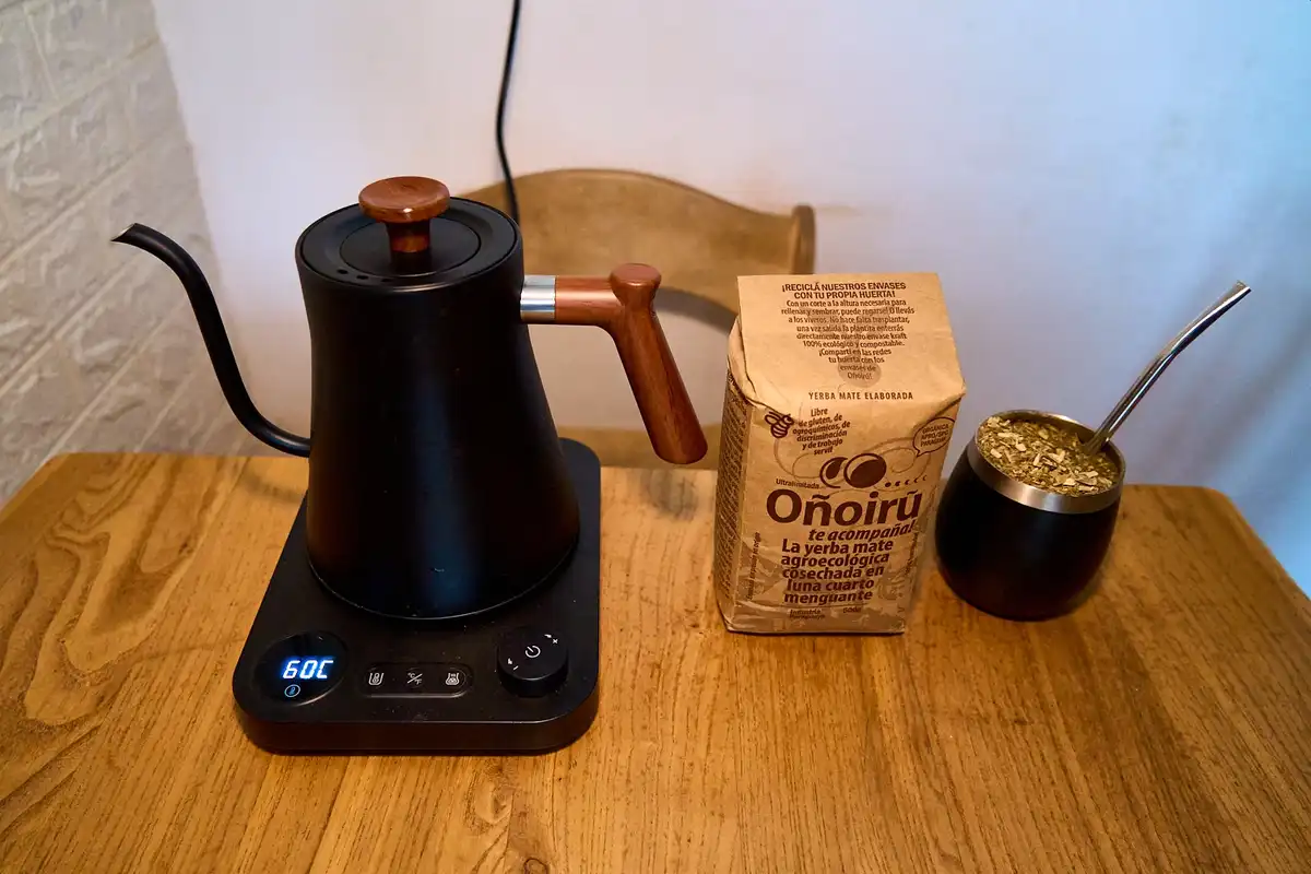 A black electric kettle with a wooden handle and spout sits on a wooden table, its digital display showing '60C'. Beside it…