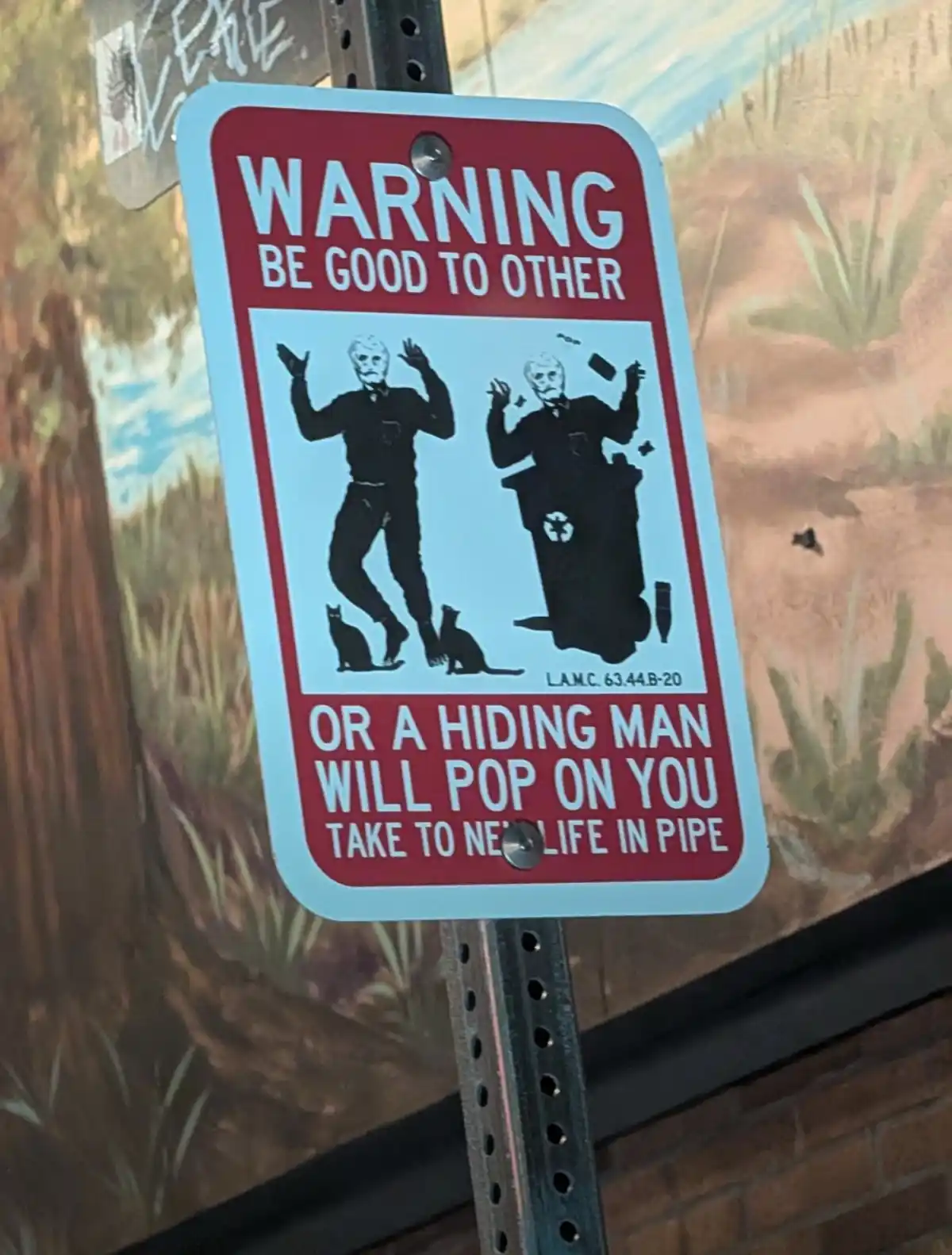 A red and white warning sign features two black silhouettes of men in masks, one standing with cats at his feet and the…