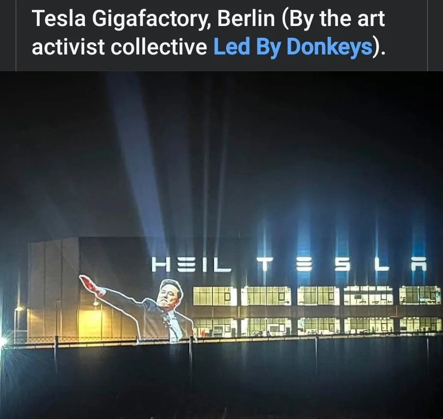 A nighttime photo of the Tesla Gigafactory in Berlin, where the building's facade is illuminated with the words 'HEIL TESLA'…