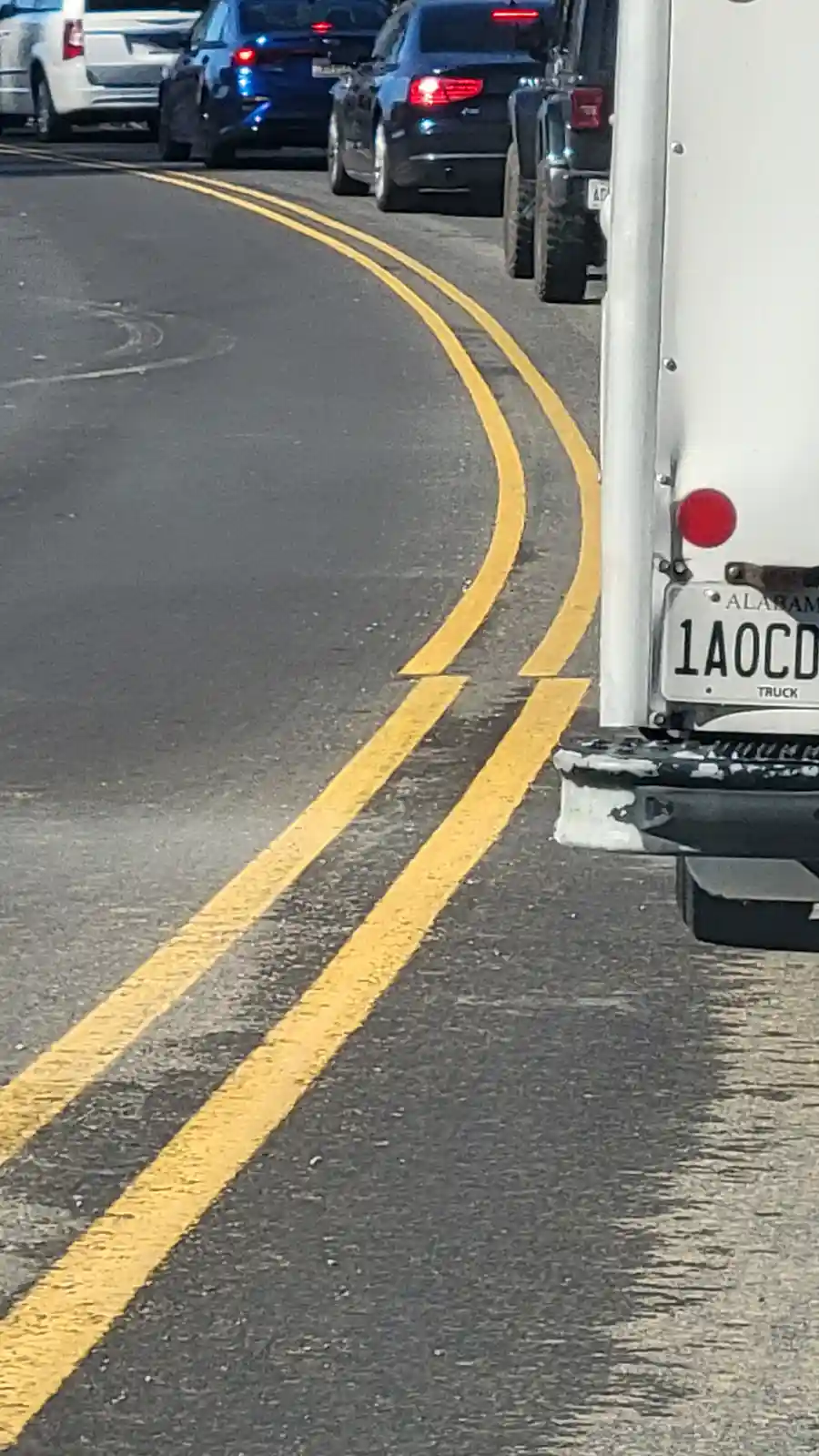 A low-angle shot of a white truck's rear bumper and Alabama license plate reading '1A0CD TRUCK', parked beside double yellow…