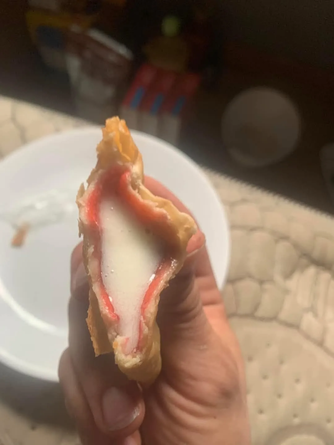 a hand holds a half-eaten, golden-brown fried food item with a white, creamy interior and a red border, resembling a crab…