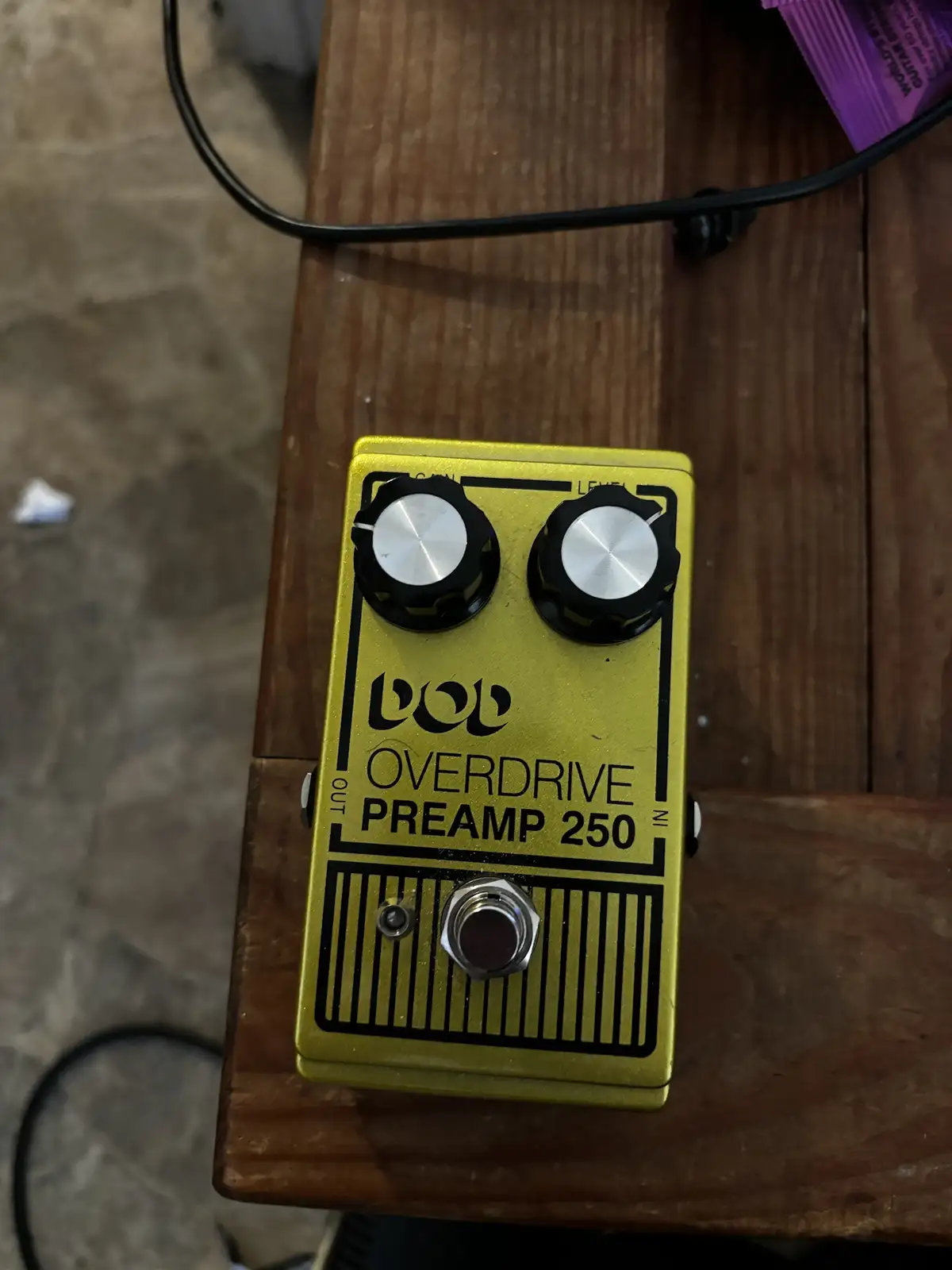 A yellow BOSS Overdrive Preamp 250 guitar effects pedal with two knobs and a footswitch sits on a wooden surface. The…