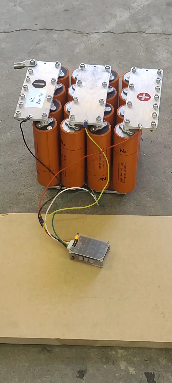 An array of orange cylindrical sodium-ion batteries arranged in a grid, connected by wires to a small electronic device with…