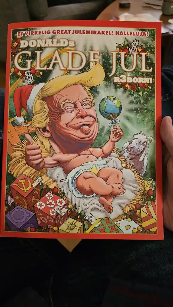 A person holds a Danish comic book cover depicting a caricature of Donald Trump as a baby in a nativity scene, wearing a…