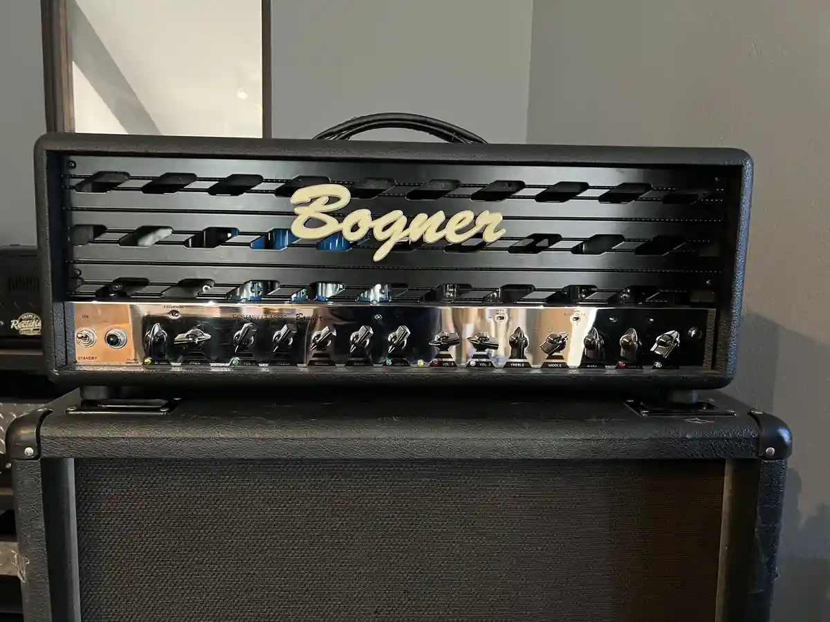 A close-up photo of a black Bogner Ecstasy Classic guitar amplifier head, showing its chrome control knobs and the brand…