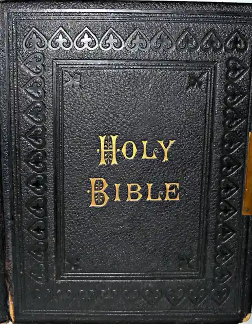 A close-up of a black, textured leather-bound book with ornate embossed borders and gold lettering that reads 'HOLY BIBLE'…