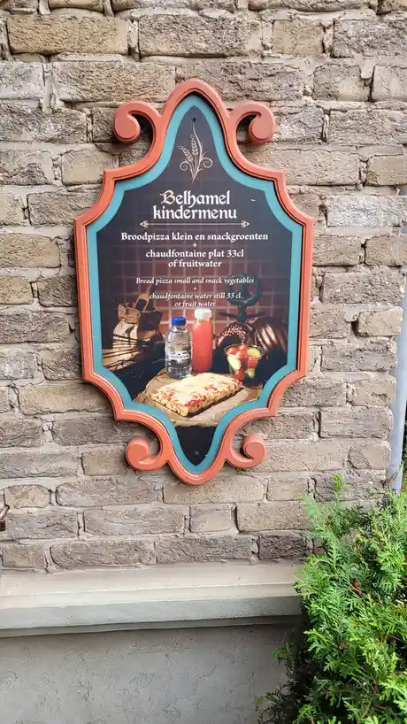 A decorative, shield-shaped menu board mounted on a stone wall displays a children's meal offering in both Dutch and…