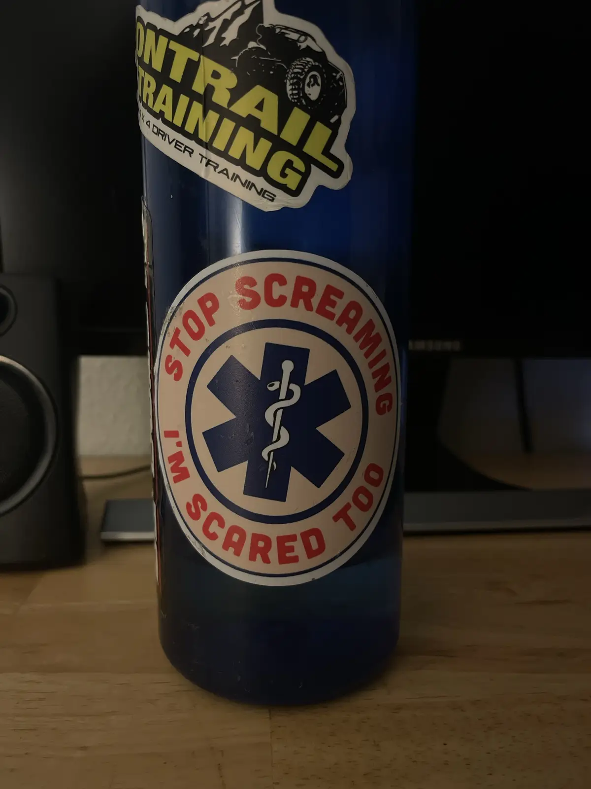 A blue water bottle has two stickers: one with a monster truck and 'OFF-TRAIL TRAINING' text, and another circular sticker…