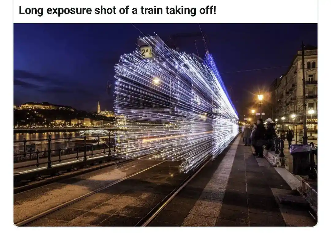 A long exposure photograph captures a tram at night, its lights streaking into bright white and blue lines across the frame…