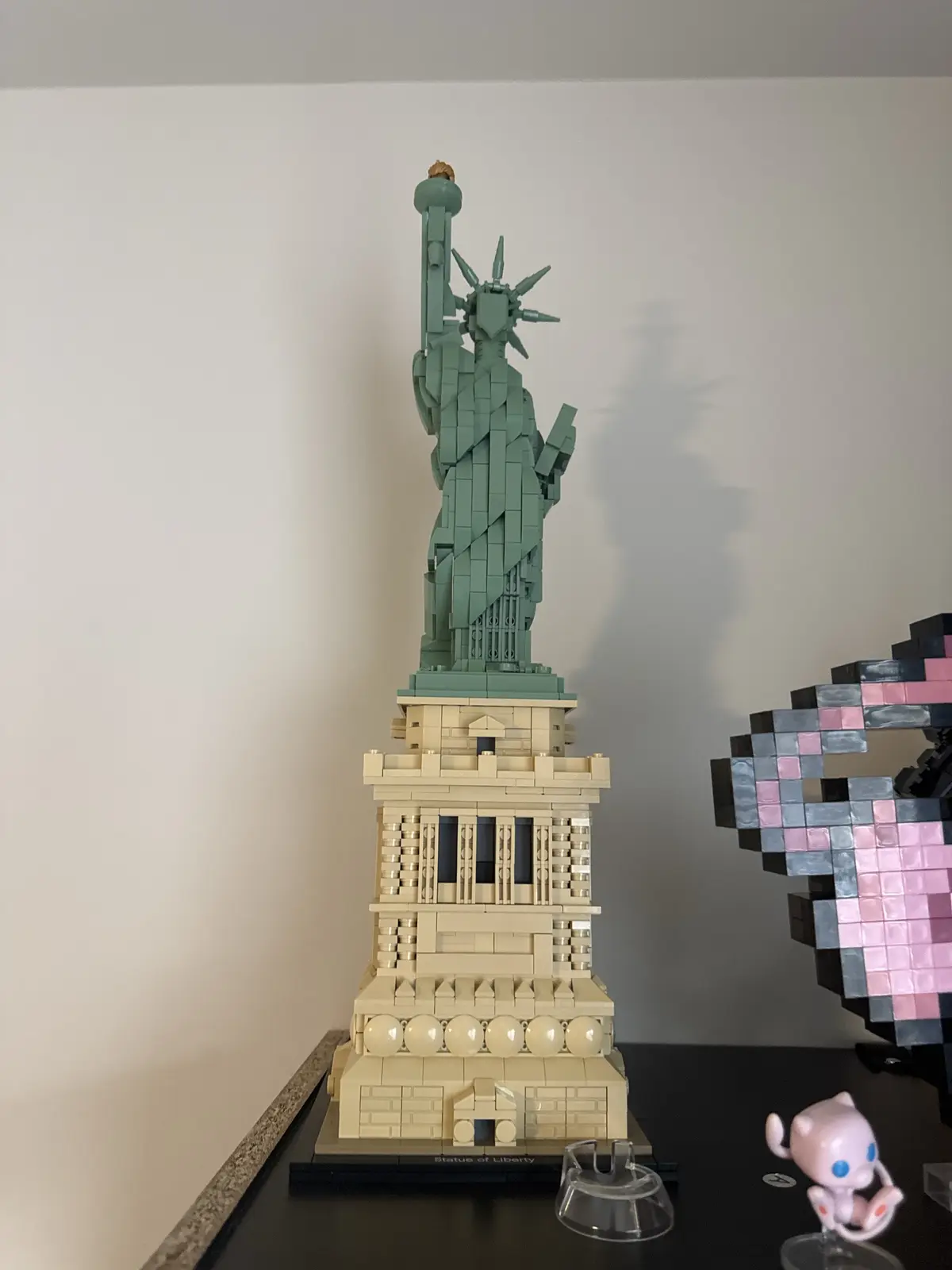 A detailed LEGO model of the Statue of Liberty stands on a black display surface, with a small pink Jigglypuff Funko Pop!…