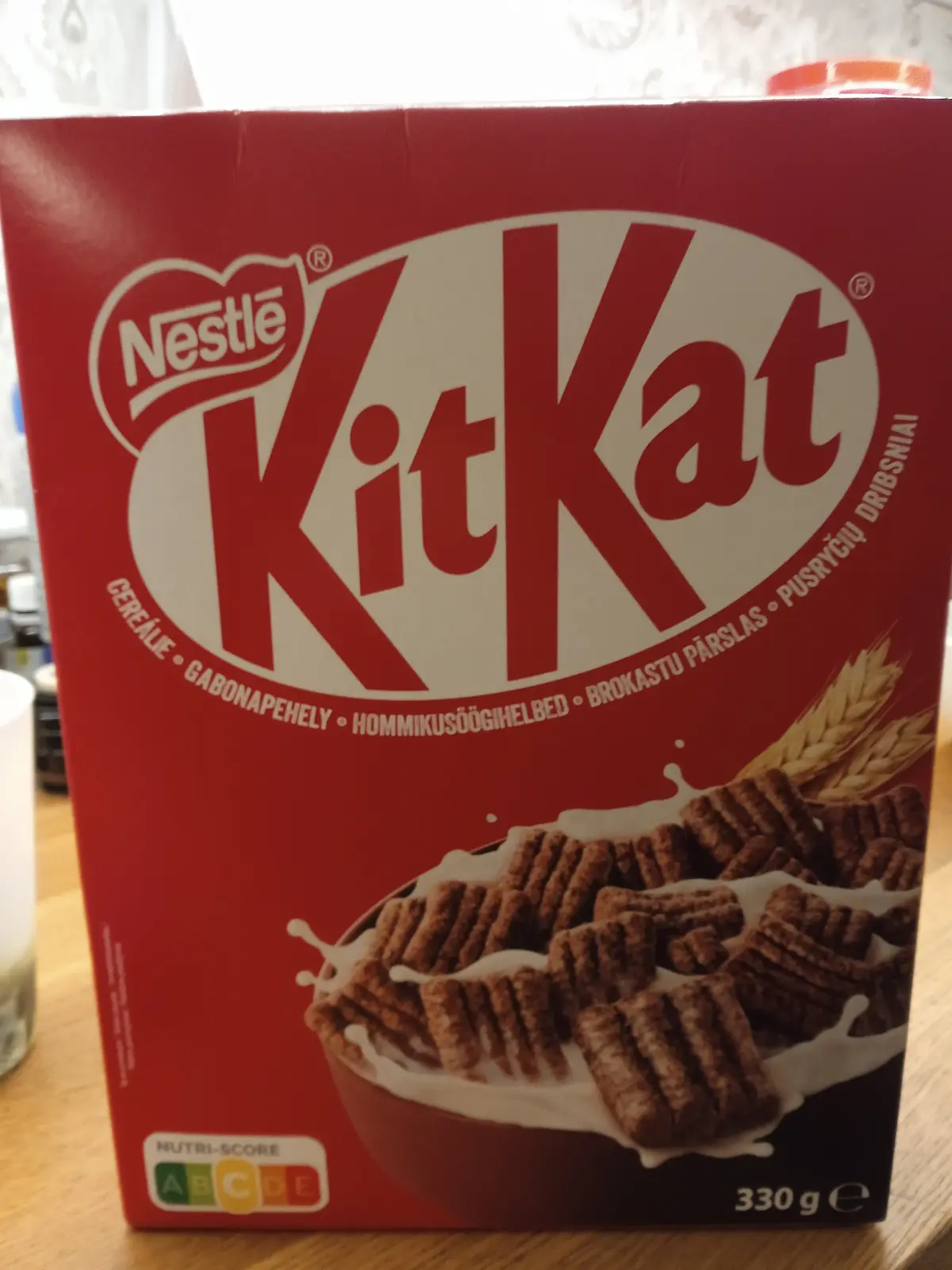 A red Kit Kat cereal box, branded by Nestlé, displays chocolate cereal pieces in a bowl with milk. The box features…