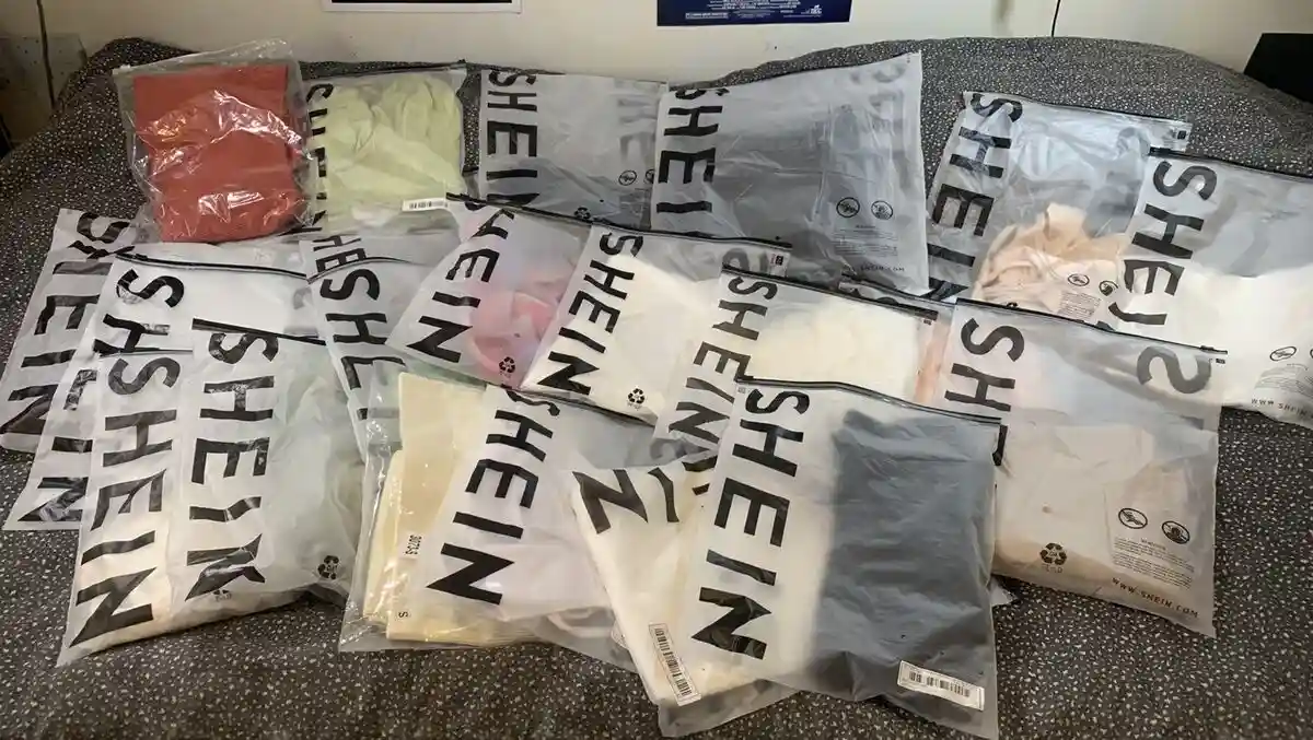 A large pile of transparent plastic bags, each prominently displaying the brand name 'SHEIN' in bold black letters, are…