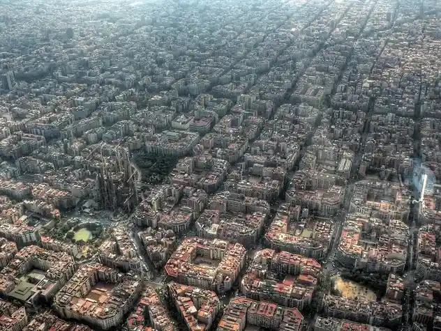 An aerial view of a dense urban grid with a prominent, partially constructed cathedral with spires and cranes visible near…