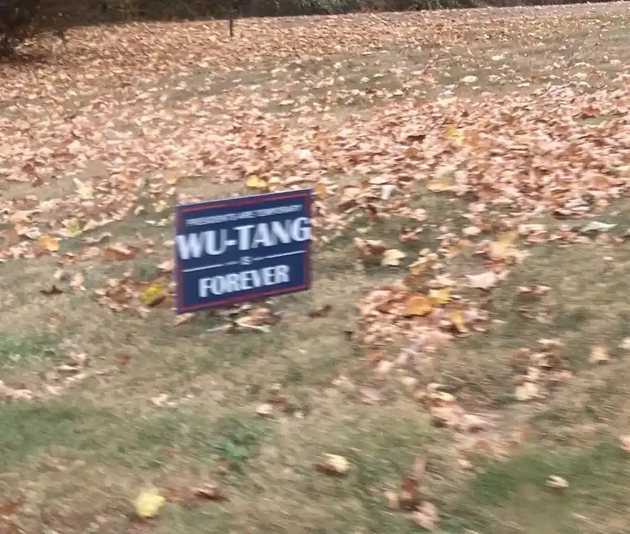A blue political-style yard sign reading 'WU-TANG IS FOREVER' with smaller text above saying 'PRESIDENTS ARE TEMPORARY' is…
