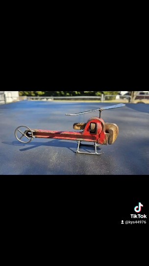 a red pipe wrench is creatively modified to resemble a helicopter, complete with a rotor blade and landing skids, resting on…