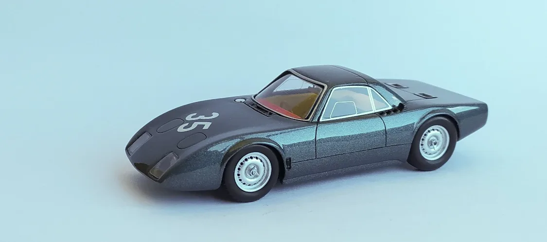 A small-scale model of a sleek, dark grey vintage race car with the number 35 on its hood, photographed against a plain…