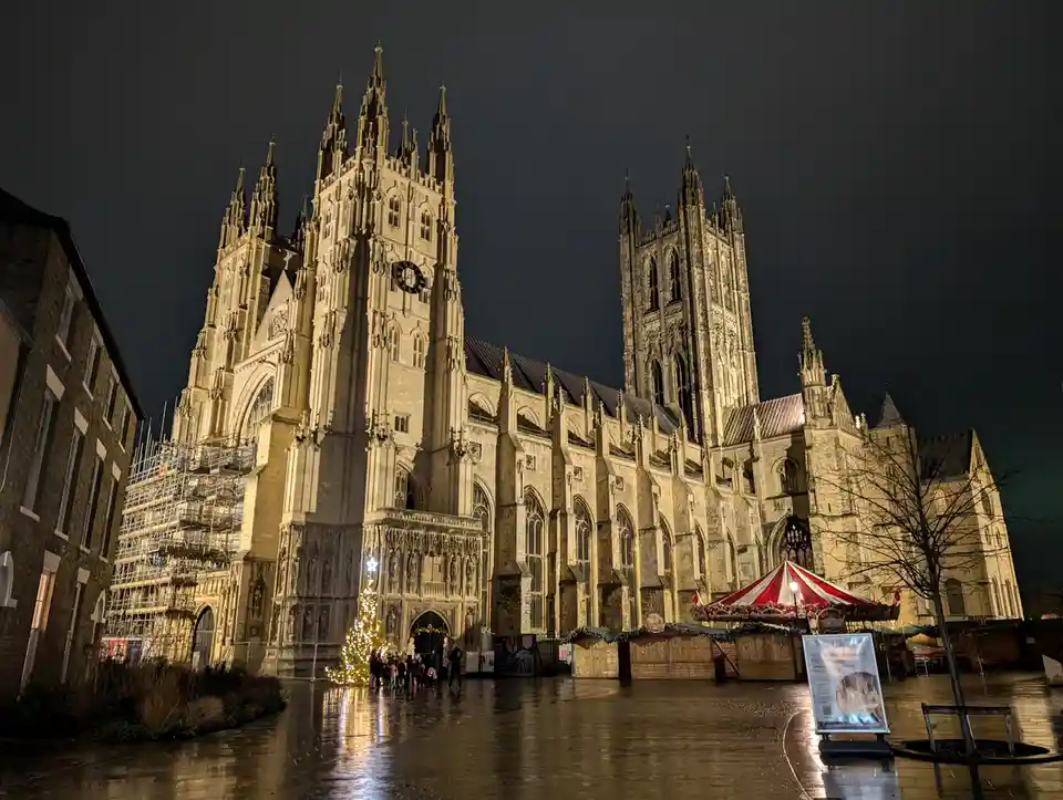 A nighttime photo of a large, ornate Gothic cathedral with multiple spires, illuminated against a dark sky. In front of the…