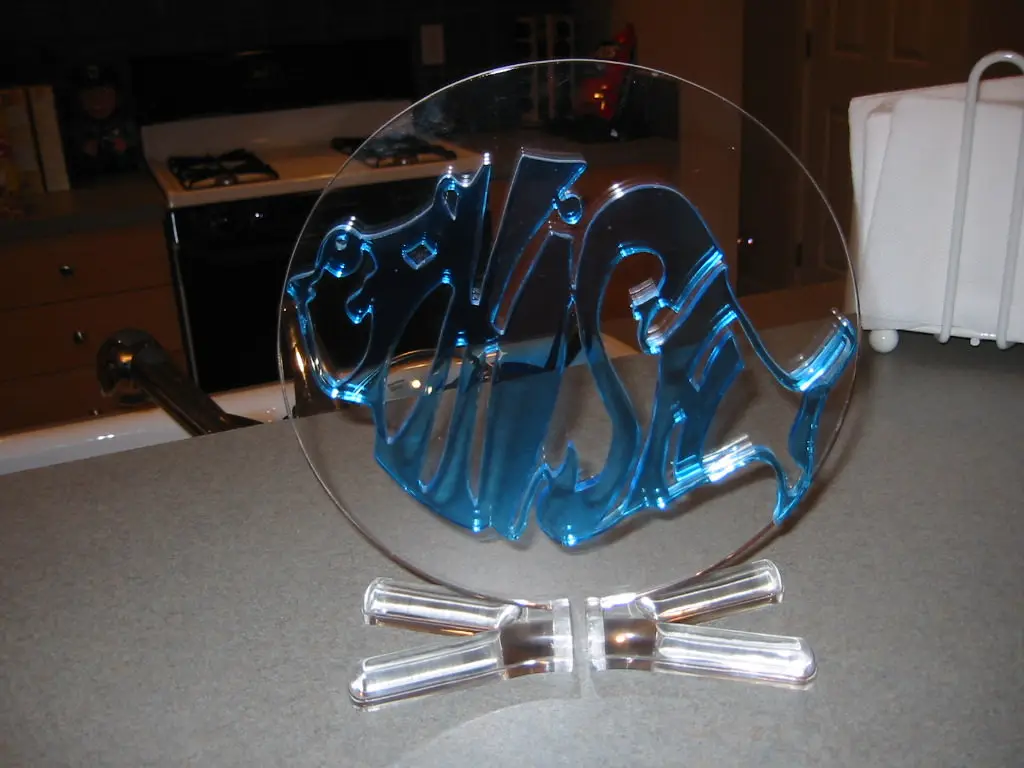 A clear glass plate with blue, stylized lettering spelling 'this is not a plate' sits on a kitchen counter, with two clear…