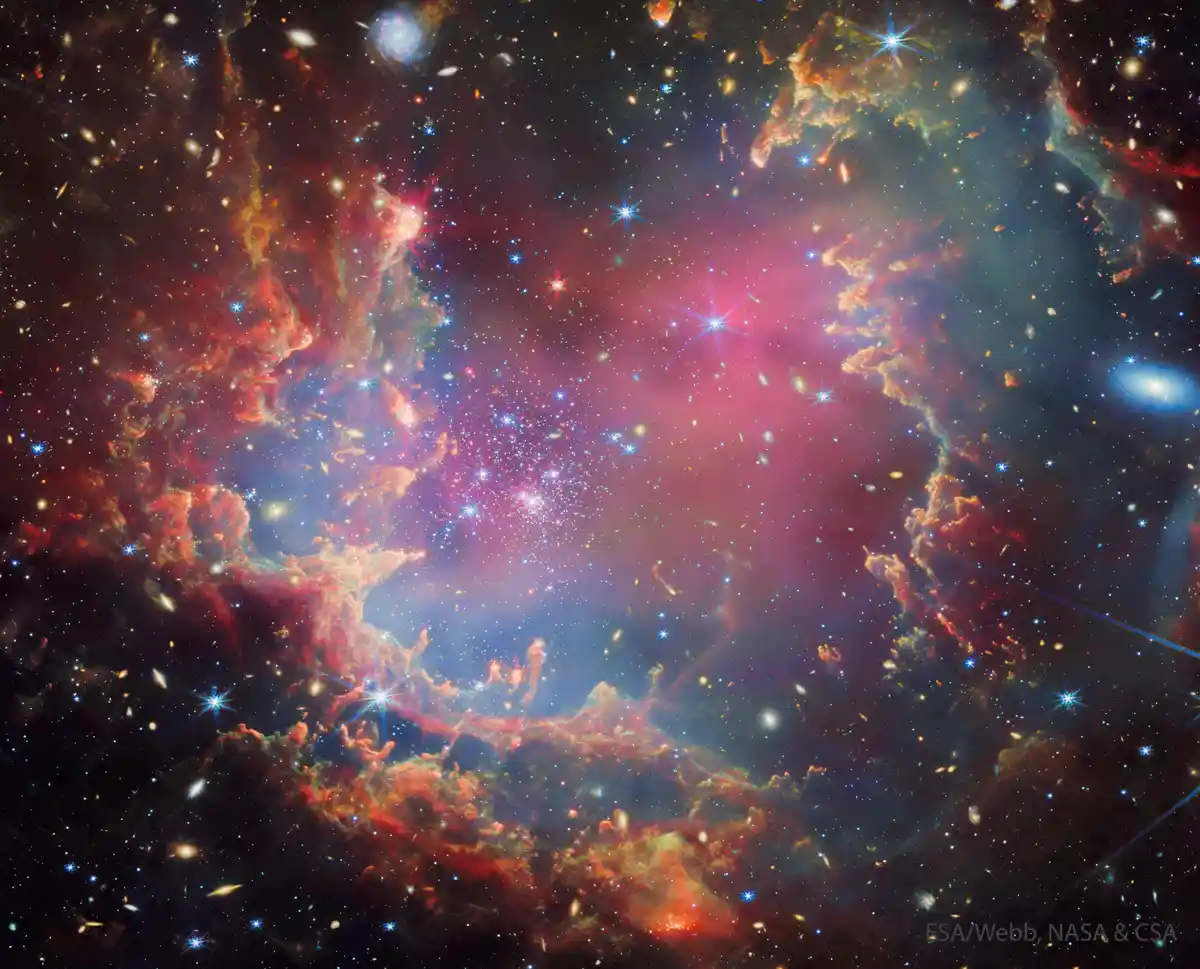 A vibrant, colorful space image showing swirling nebulae in reds, blues, and purples, filled with countless stars and…