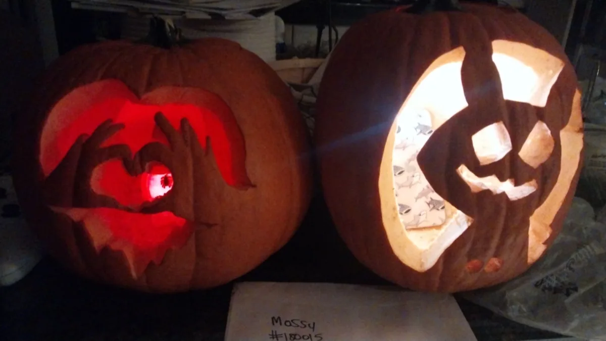 Two carved pumpkins sit side by side, one glowing with a heart-shaped cutout and hands forming a heart, the other with a…