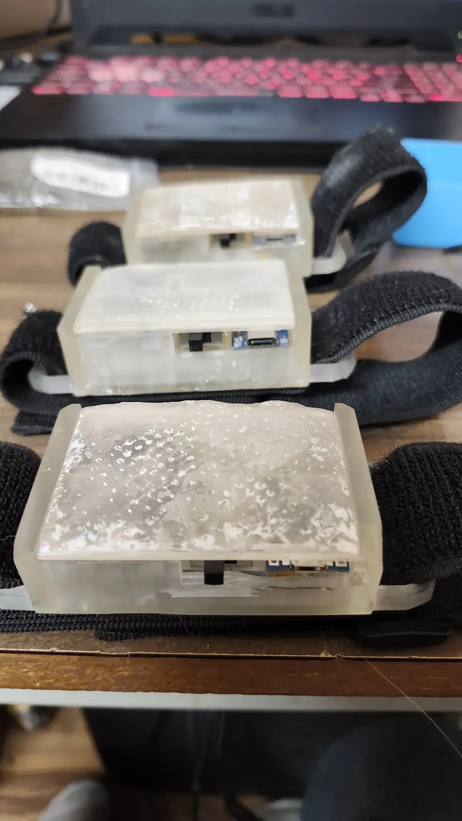 Three small, translucent plastic cases, each housing a circuit board with visible ports, are arranged in a row on a wooden…