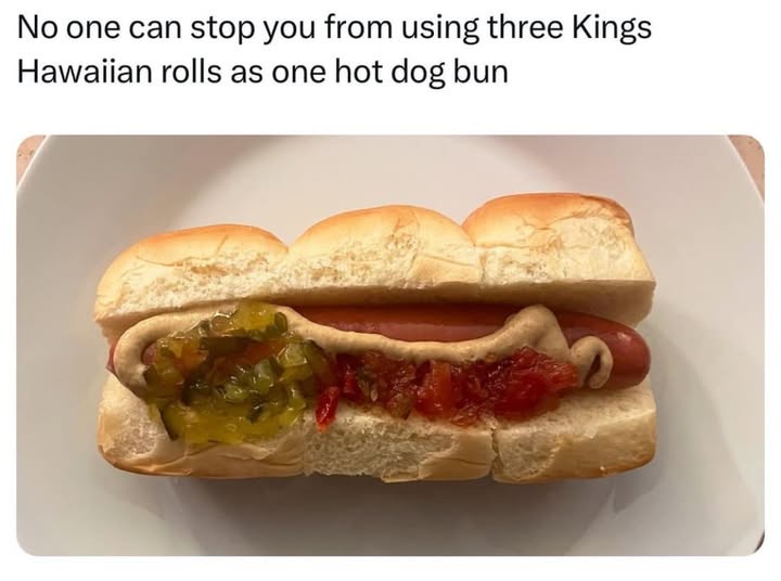 A hot dog sausage sits in a bun made from three Kings Hawaiian rolls stacked together, topped with mustard, relish, and…