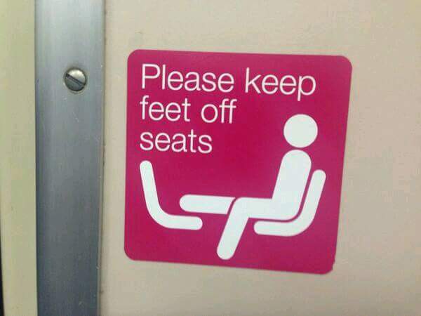 A pink public transit sign with white text and iconography instructs passengers to 'Please keep feet off seats,' accompanied…