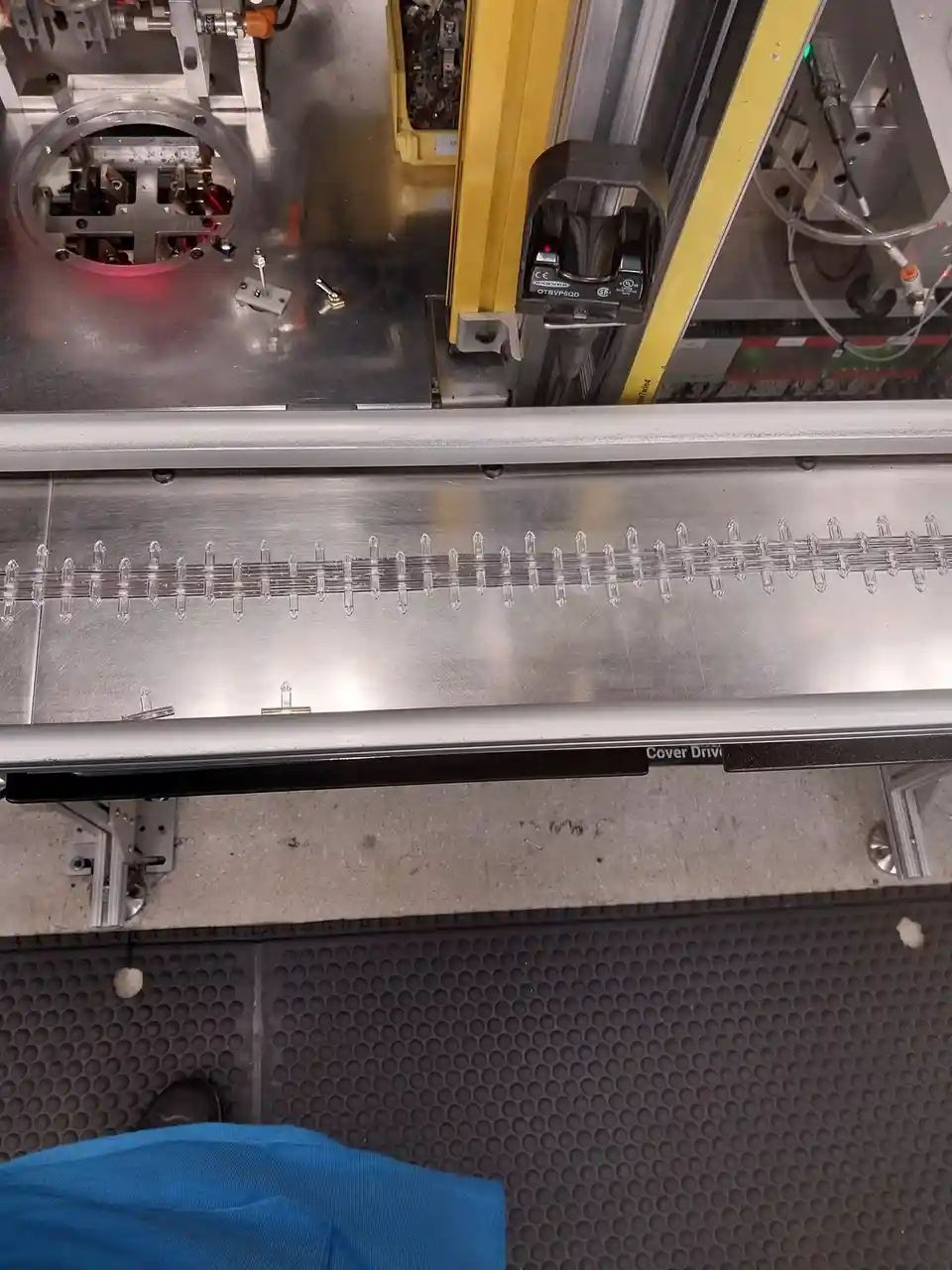 A close-up photo of an industrial machine's conveyor belt with clear plastic clips arranged in a row, showing a person's…