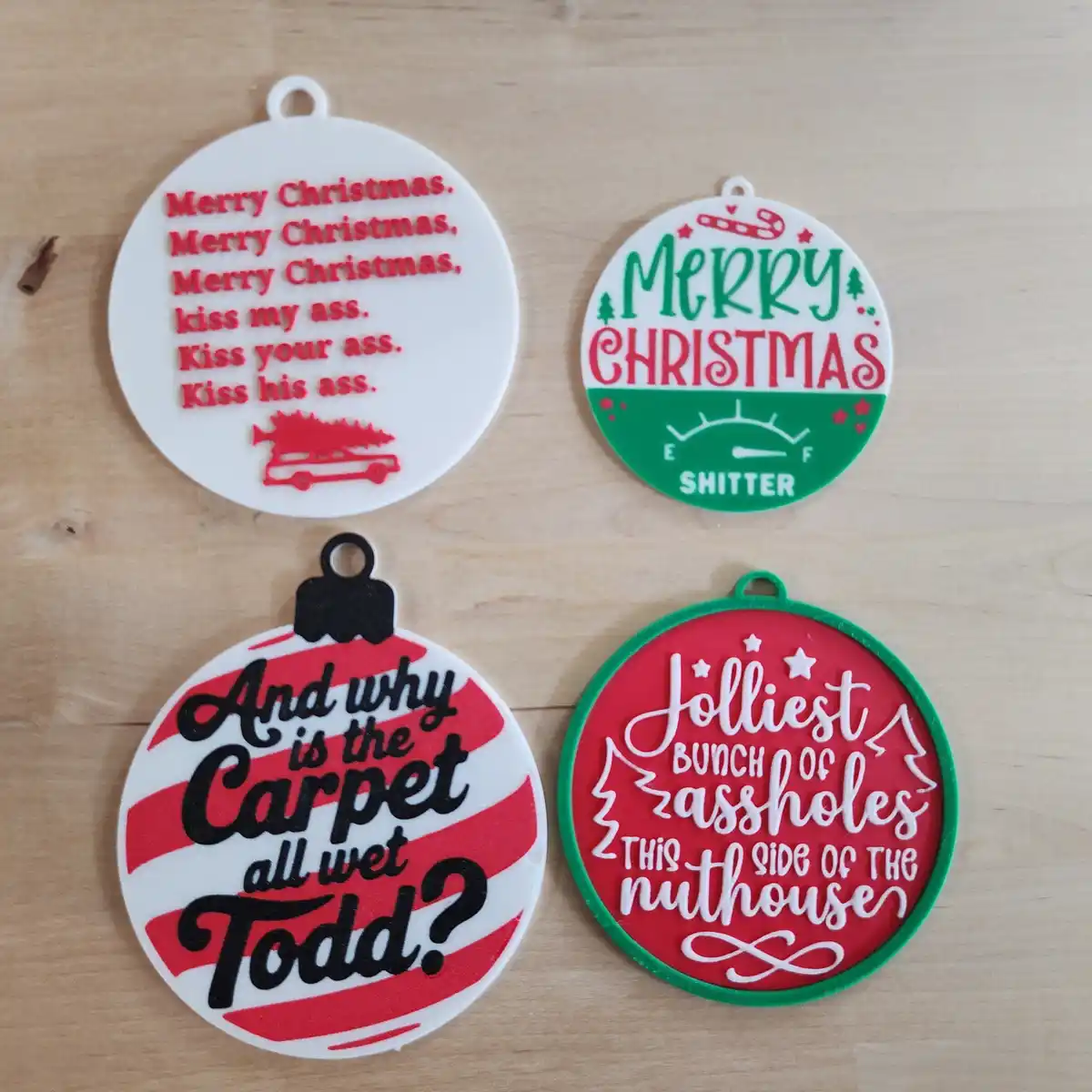 Four 3D-printed Christmas ornaments with crude, humorous text. One reads 'Merry Christmas. Merry Christmas, Merry Christmas…