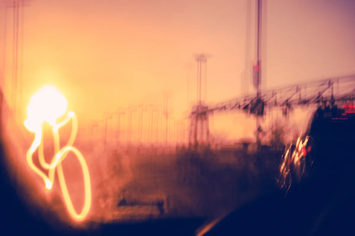A blurry, motion-blurred photograph taken from inside a vehicle at night, showing streaks of orange and yellow light. A…