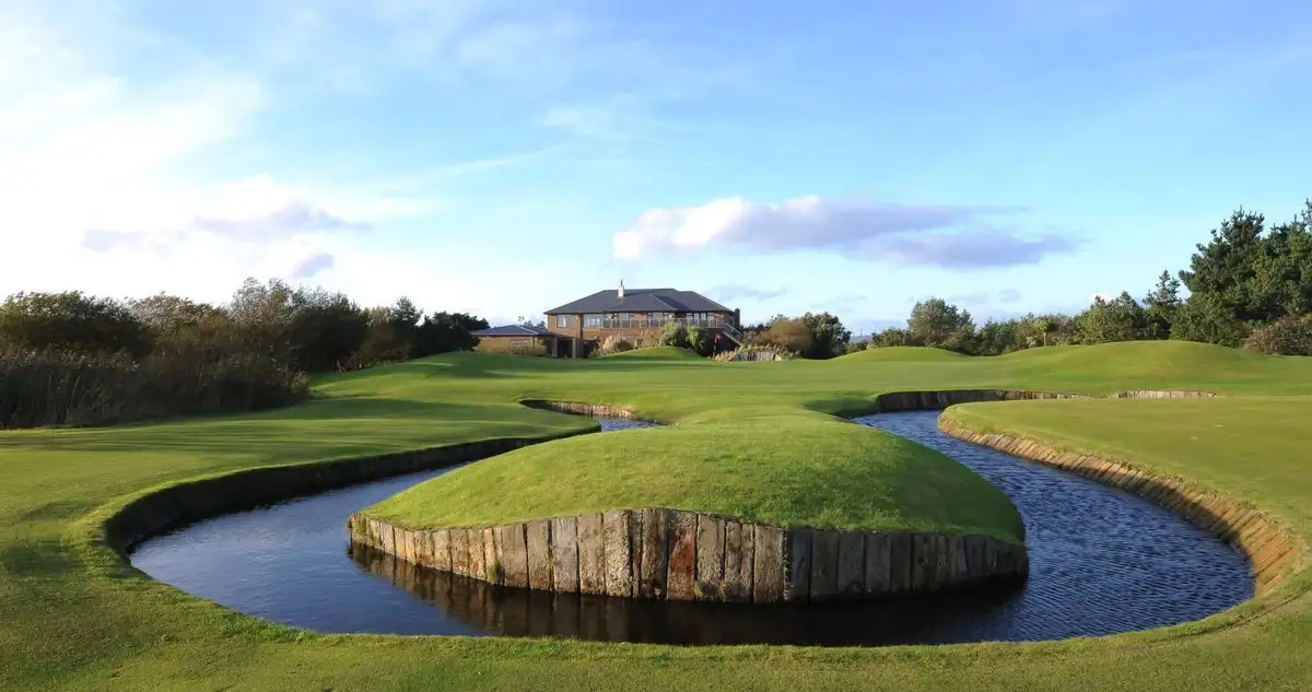 a scenic golf course with a winding water hazard surrounding a grassy island, a house visible in the background under a…