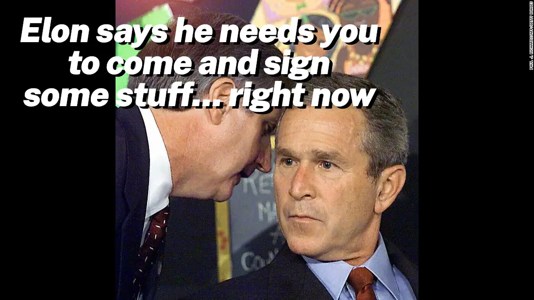 A man in a suit leans in conspiratorially to whisper to another man in a suit, who looks skeptical and unimpressed. The…