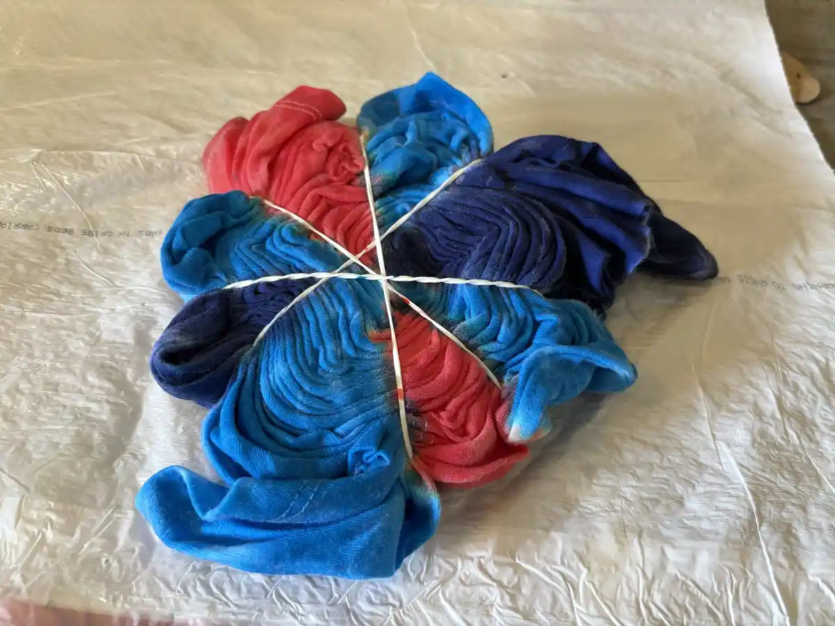 A shirt is tightly bound with white rubber bands in a criss-cross pattern, creating distinct sections dyed in vibrant red…