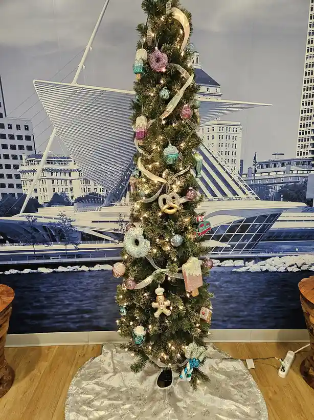 A tall, decorated christmas tree with lights and ornaments shaped like donuts, cupcakes, pretzels, and popsicles stands…