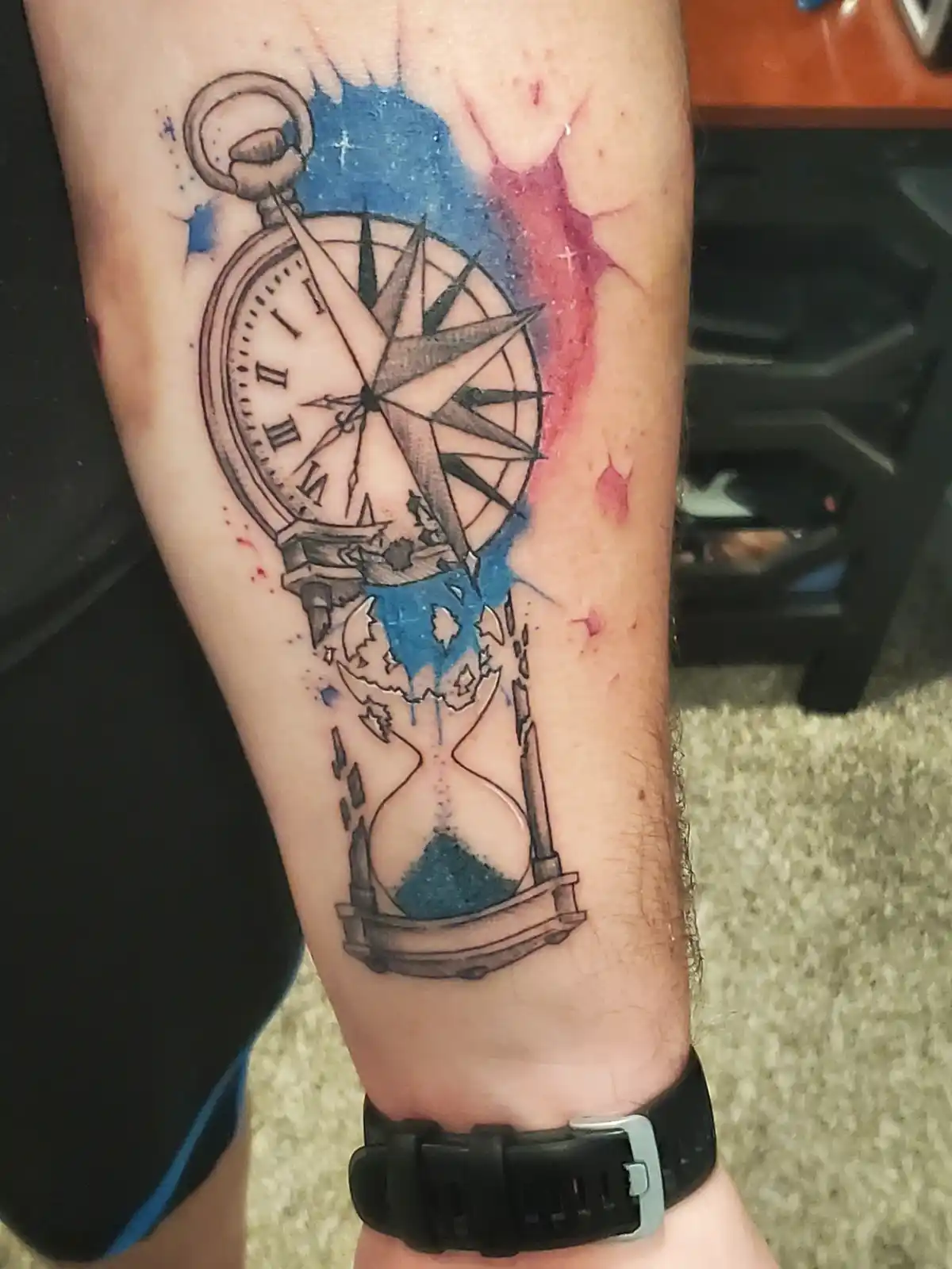 A close-up photo shows a tattoo on a person's forearm featuring a pocket watch with a compass rose inside its face, which is…