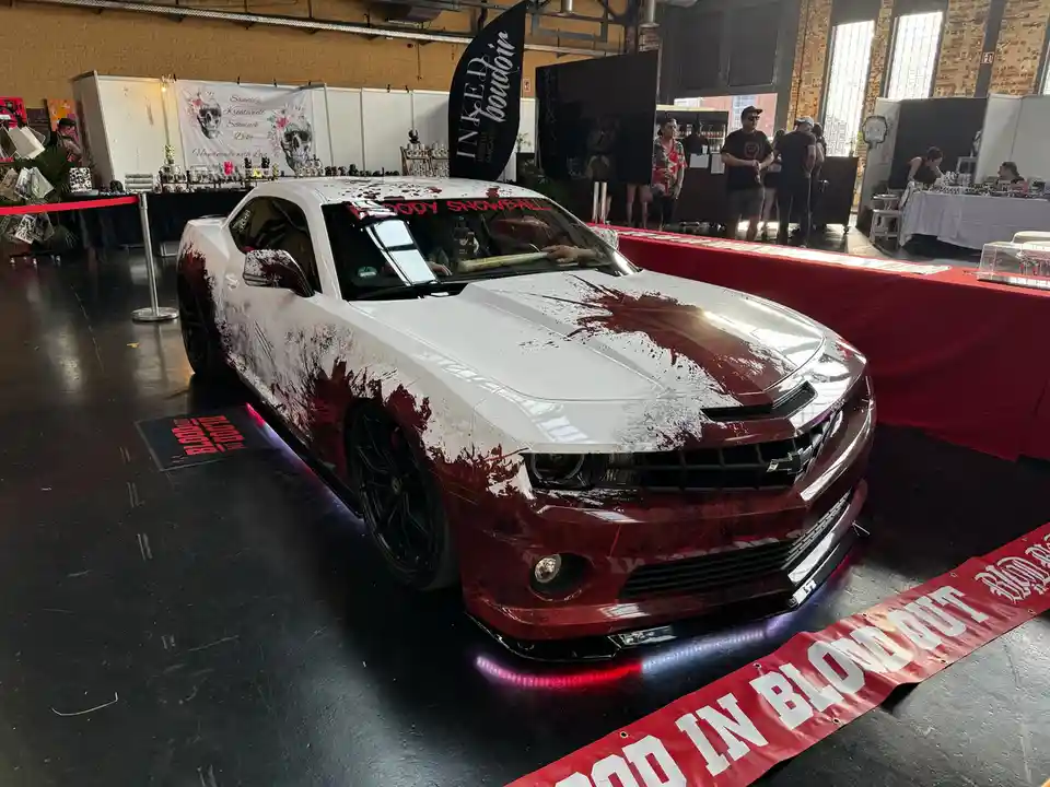 A white and red Chevrolet Camaro with a custom 'bloody' paint job featuring red splatter effects and the text 'BLOODY…