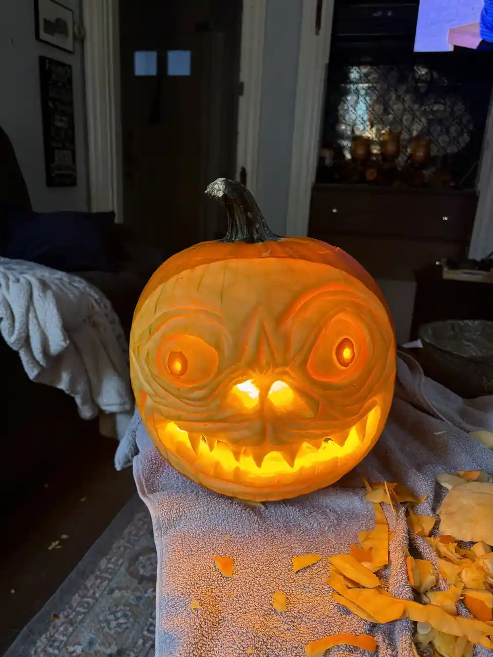 A close-up photo shows a intricately carved, glowing jack-o'-lantern with wide, swirling eyes and a jagged, toothy grin…