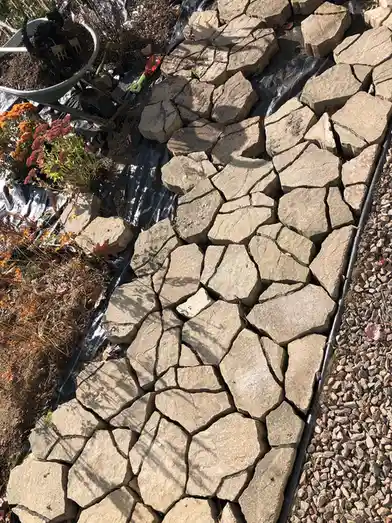 An overhead photo shows a garden path made of irregularly shaped, light-gray stones laid in a rough pattern over black…