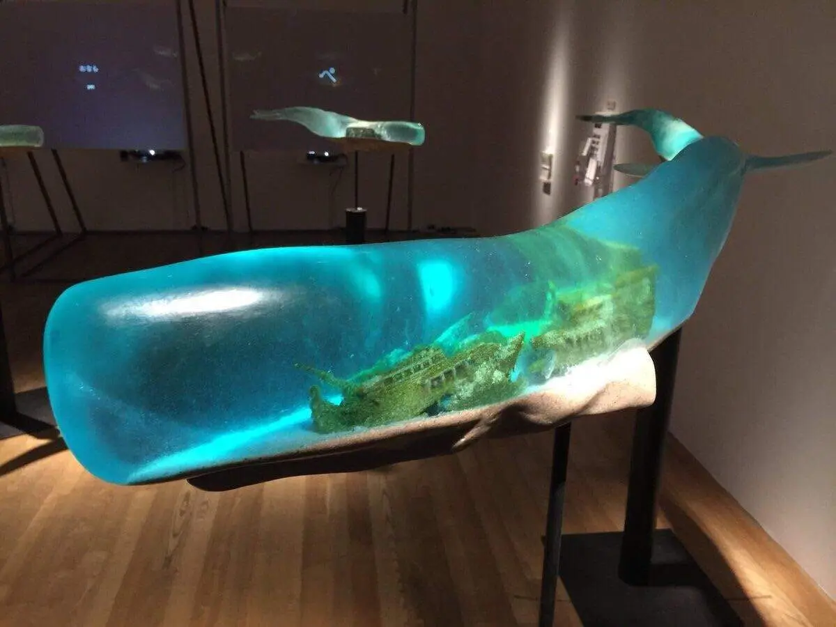 A large, translucent blue whale sculpture is displayed on a stand in a museum-like setting, with the interior filled with…
