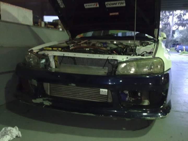 A car with its hood open and front bumper removed, revealing a large aftermarket radiator installed in place of the bumper…