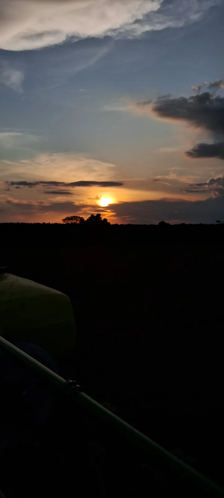 A photo taken from inside a vehicle, likely a tractor, looking out at a dramatic sunset with the sun low on the horizon…