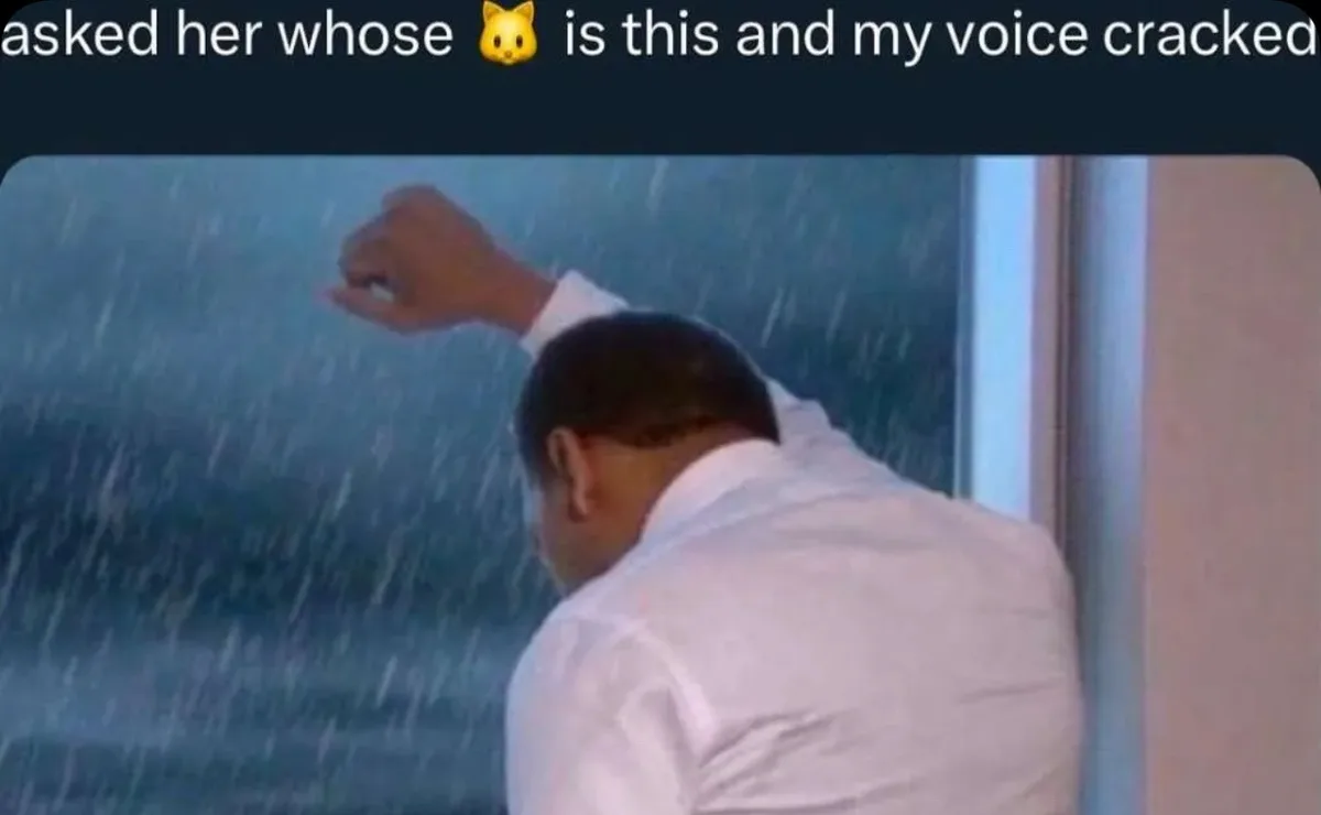 A man in a white shirt is seen from behind, looking out a window at heavy rain while raising his right hand in a gesture of…